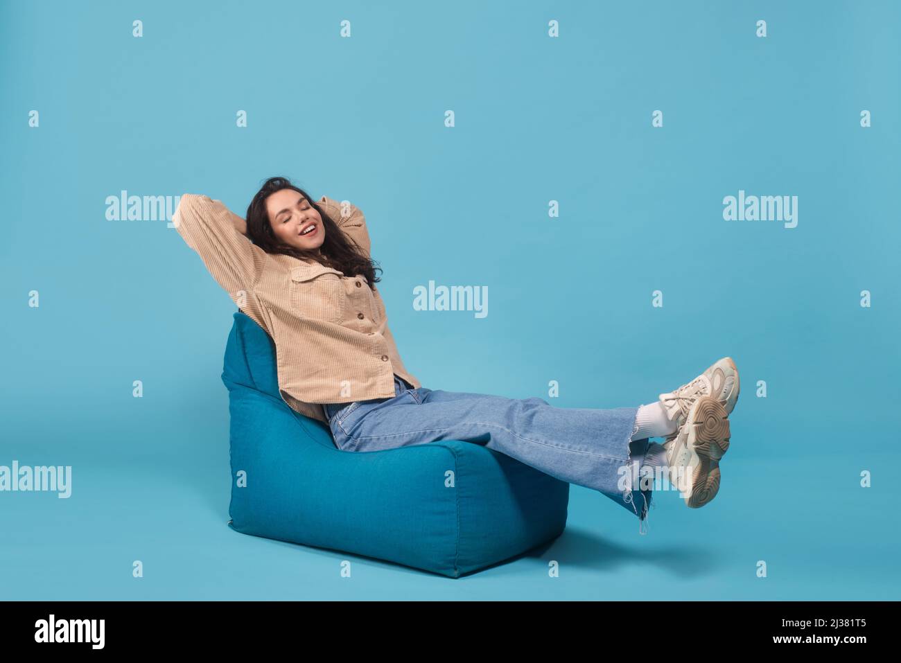 Satisfied happy millennial european woman in casual relaxes and enjoys rest on bagchair isolated on blue background Stock Photo