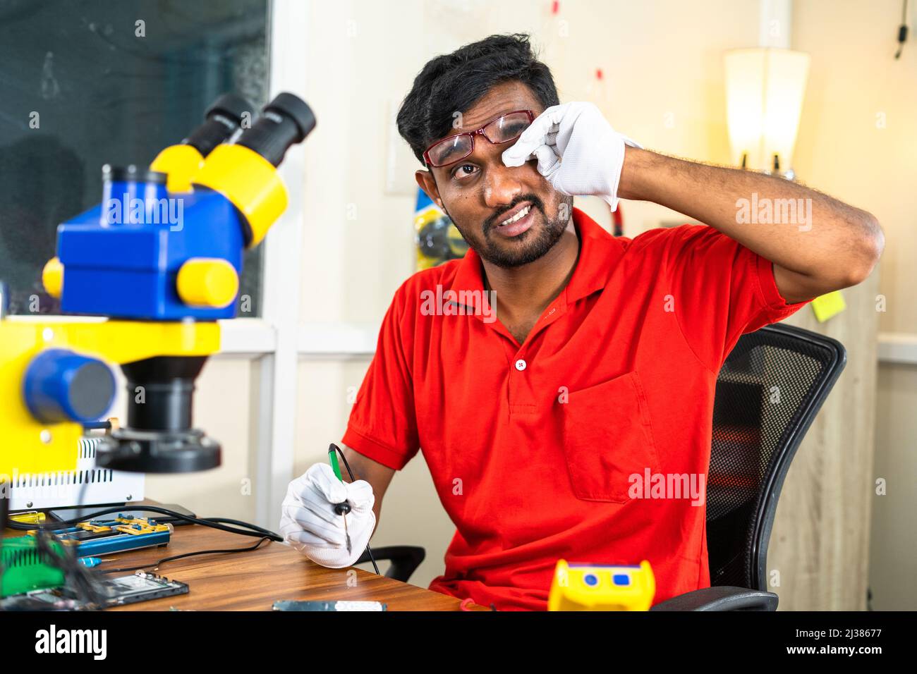 repairman got taired while reparing mobile phone showing by rubbing eyes at service cente - concept of concept of hard worker, skill labour and health Stock Photo