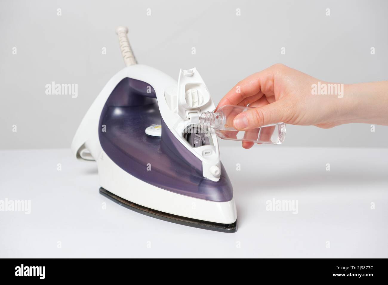 A woman pours a cleansing liquid into a water tank in an iron. Cleaning