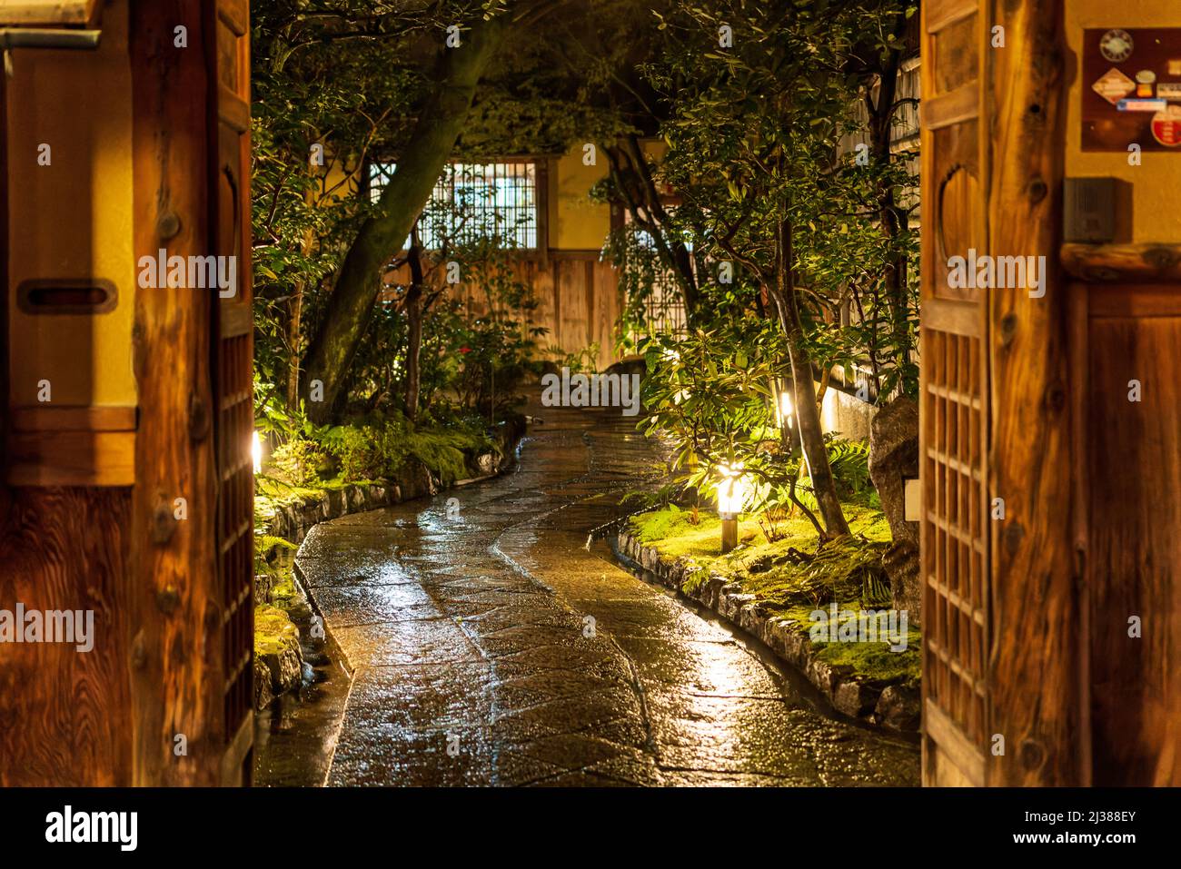 Wooden gates open to Japanese garden at night after rain Stock Photo
