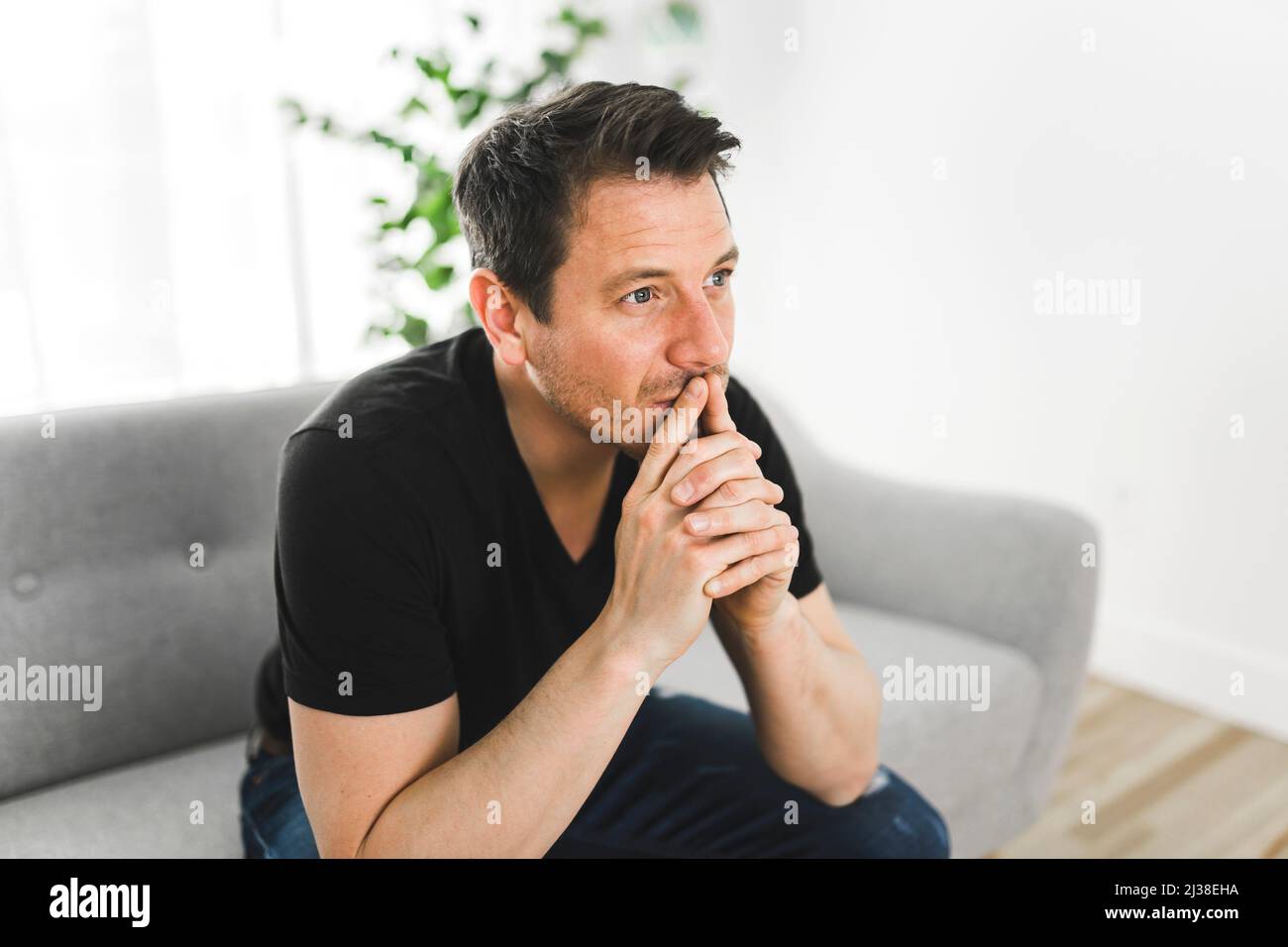 Depressed and thinking man thinking at home on couch Stock Photo