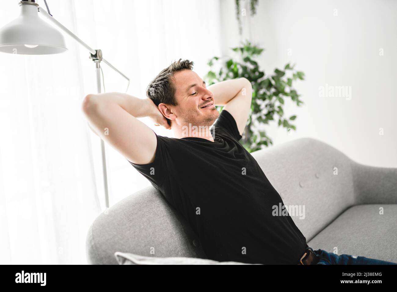 Relaxing man and dreaming on sofa at home with arm behind his head