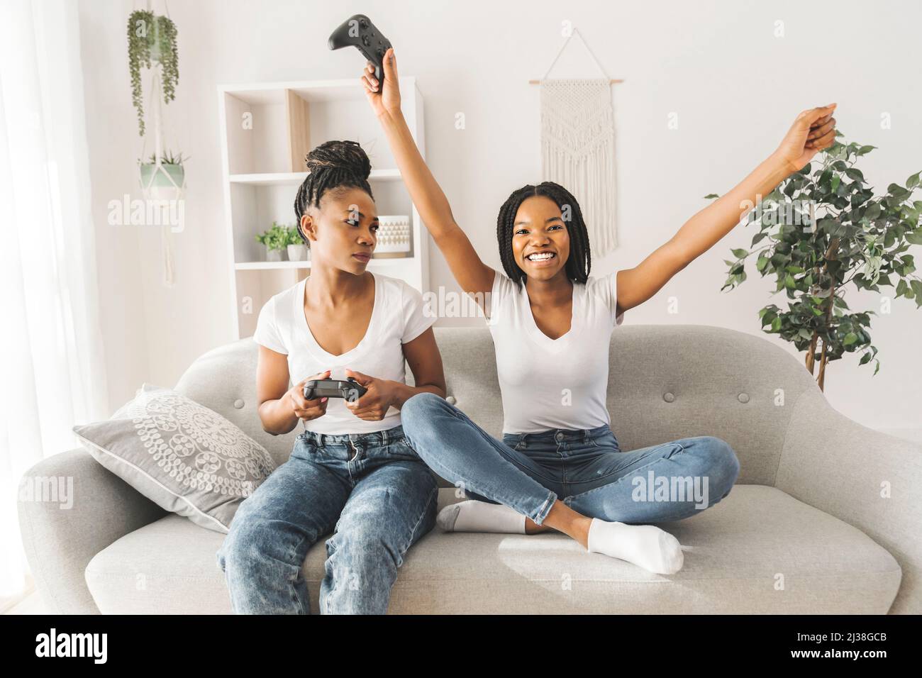 Mother and daughter sitting on sofa at home play video game together Stock Photo
