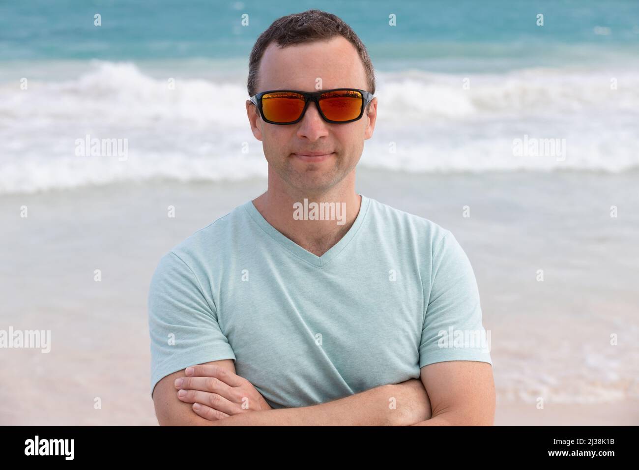 Portrait of young adult sporty smiling European man in shiny red sunglasses, outdoor photo taken on a summer beach Stock Photo