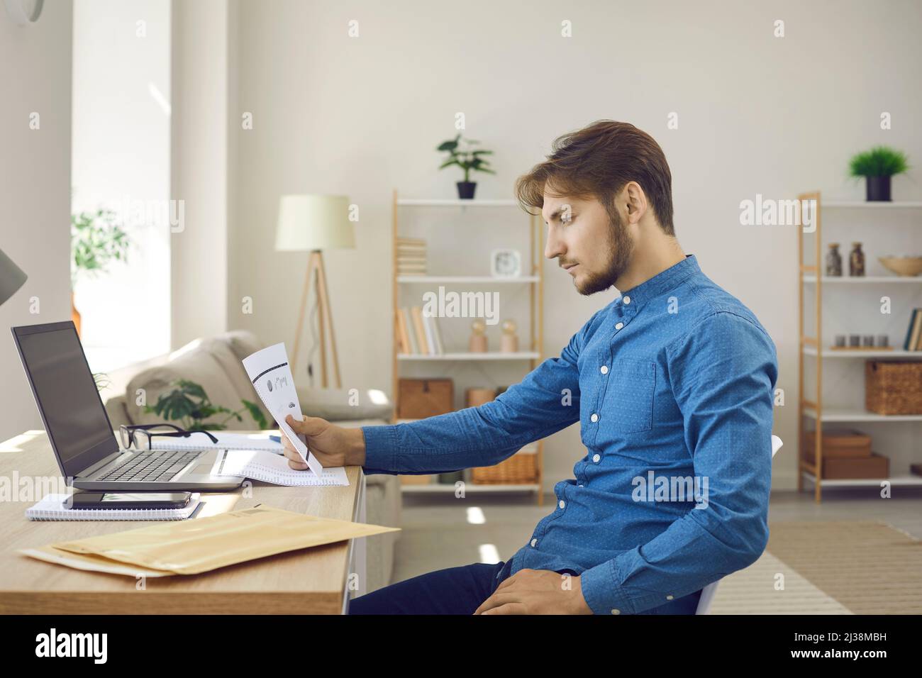 Serious man sitting at desk and reading business document he received by paper mail Stock Photo