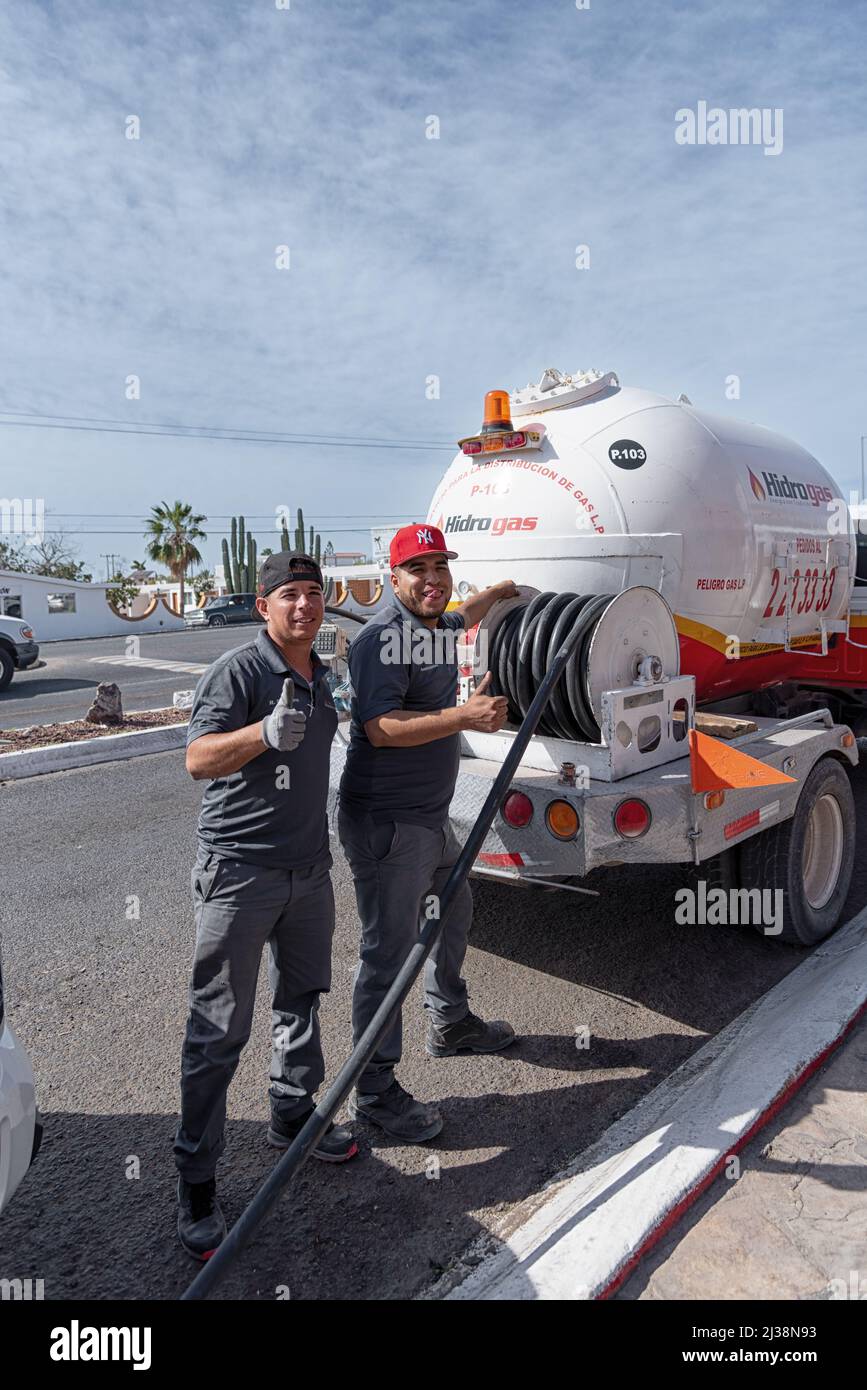 Two workers wearing clean, grey uniforms, stand by a large red and white propane truck, posing with thumbs up, in San Carlos, Sonora, Mexico. Stock Photo