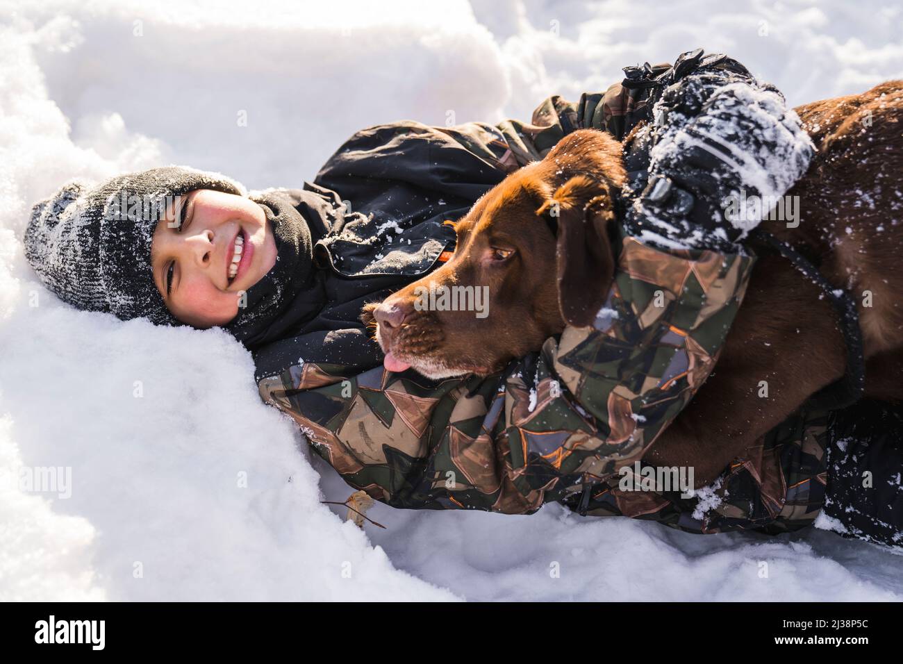 Portrait of little boy with labrador dog in winter season lay on the ground Stock Photo