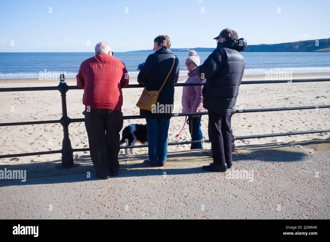 A group of people having a chat with a dog walker on Scarborough beach during on a bright winter day Stock Photo