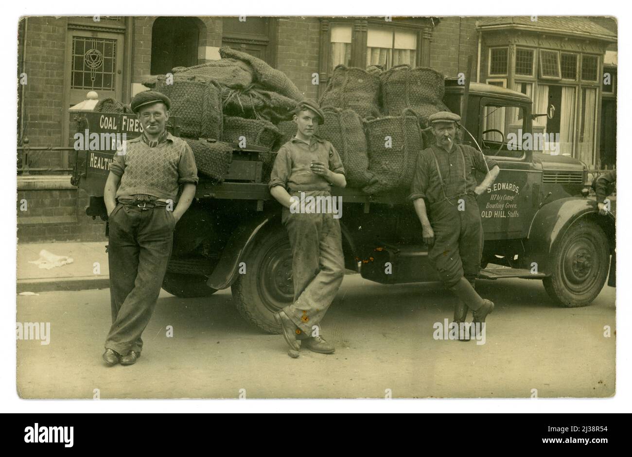 Original, clear 1930's era postcard of 3 coal merchant's delivery men and loaded truck of coal. These men are confident characters. On the delivery truck is a sign - 'S. Edwards, 117 Ivy Cottage, Bowling Green, Old Hill, Staffs' Staffordshire, West Midlands, England, U.K. (it lies within the Black Country). Stock Photo