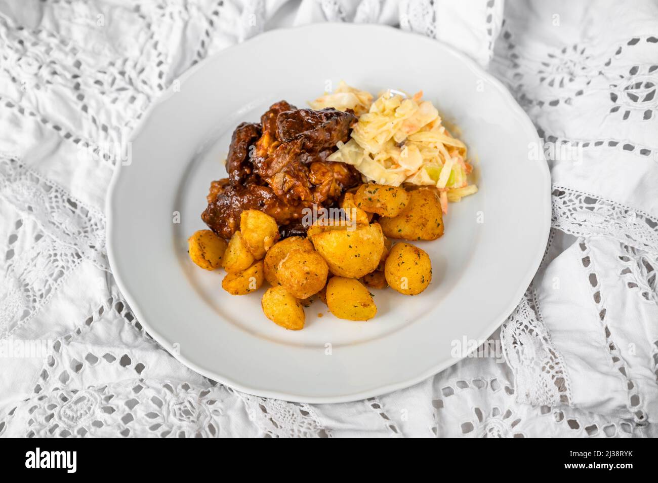 Baked sliced turkey meat in wild gypsy sauce, fried potato and salad coleslaw on white plate on white lace tablecloth. Stock Photo