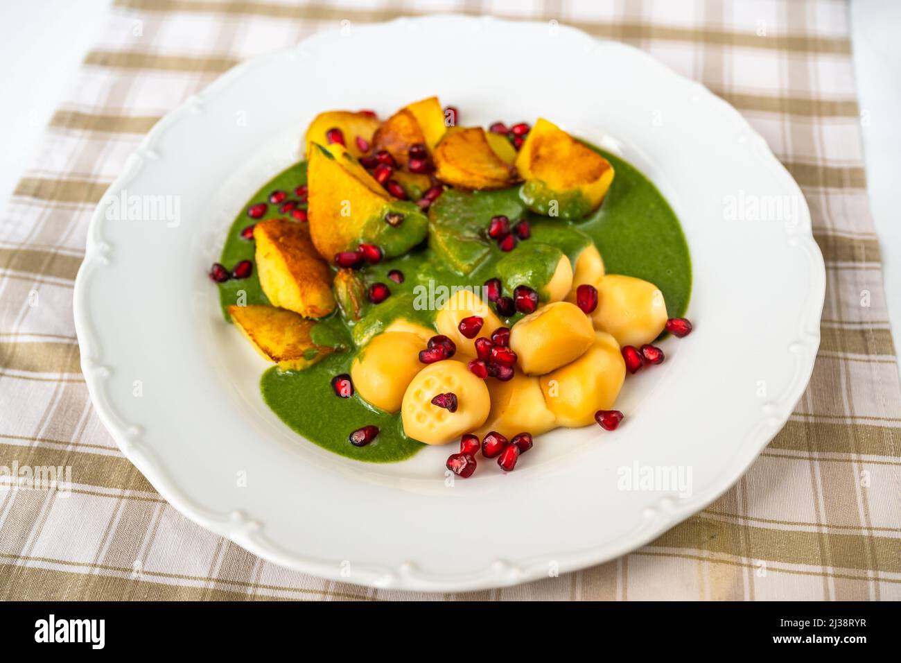 Smoked cheese balls, fried potato, spinach sauce and pomegranate seed on white plate on table. Stock Photo