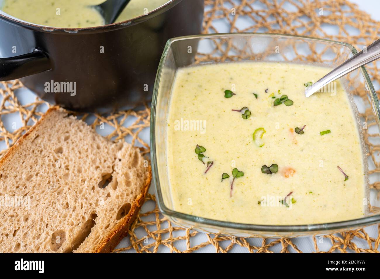 Creamy broccoli soup in glass bowl and in black pot, bread on table. Stock Photo
