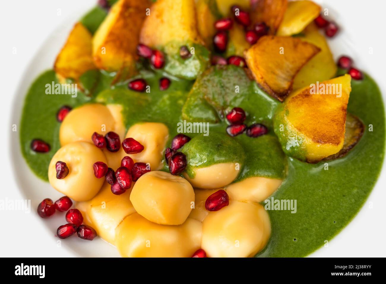 Smoked cheese balls, fried potato, spinach sauce and pomegranate seed on white plate, vegetarian dinner, closeup. Stock Photo