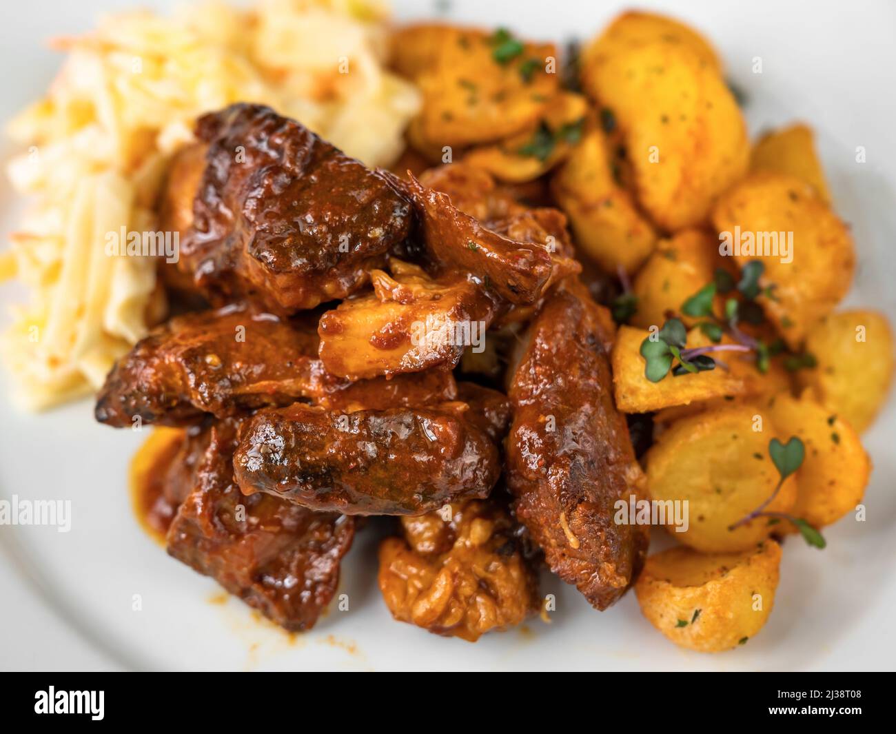 Baked marinated sliced turkey meat in wild gypsy sauce, fried potato and salad coleslaw on white plate, closeup. Stock Photo