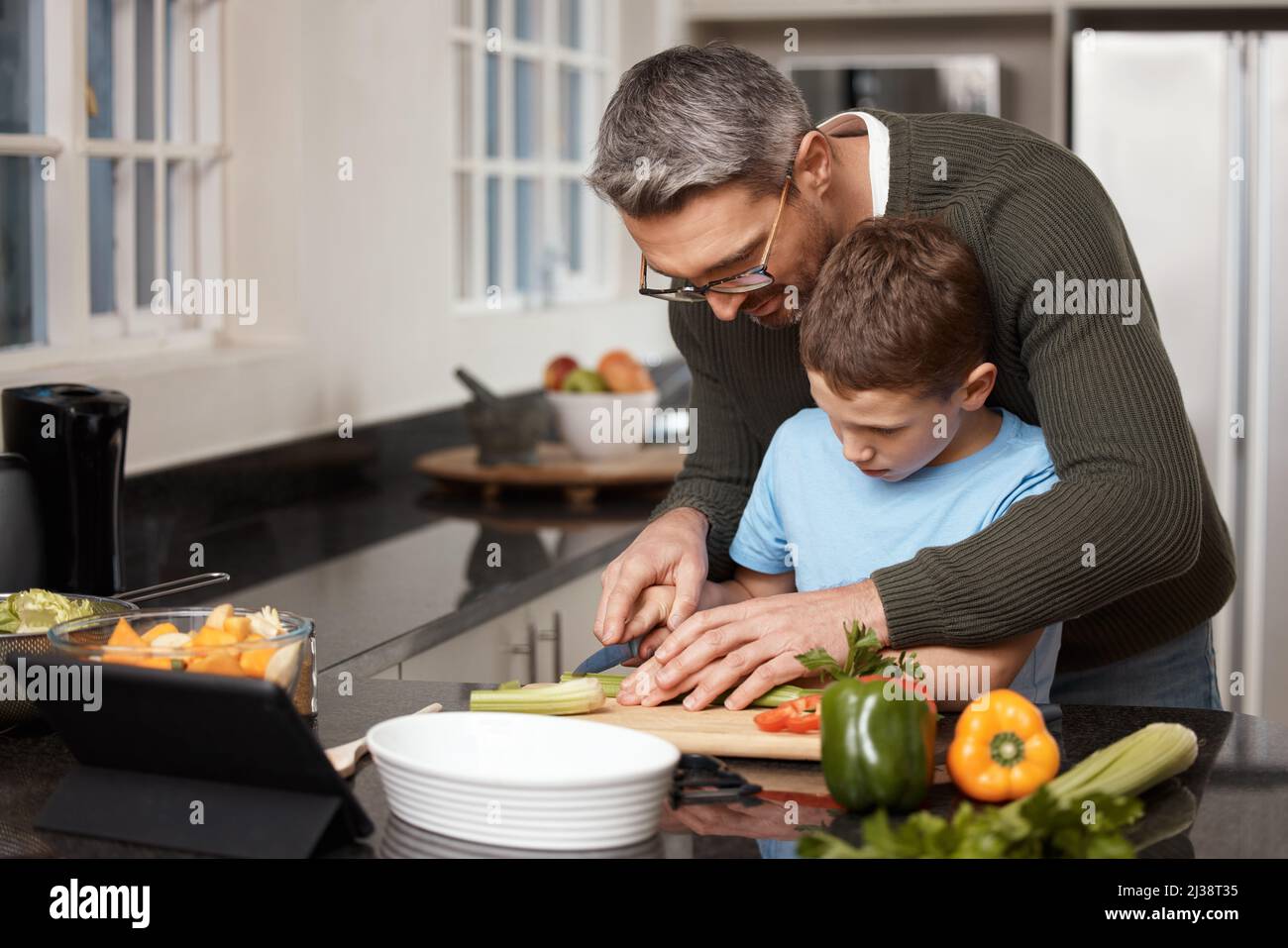 You have to be very careful not to cut yourself. Shot of a little boy cooking with his father at home. Stock Photo