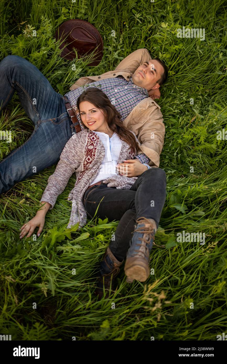Young couple having picnic in meadow on bright sunny day. Man and woman enjoy each other's company.A couple in love lies on a green meadow. Stock Photo