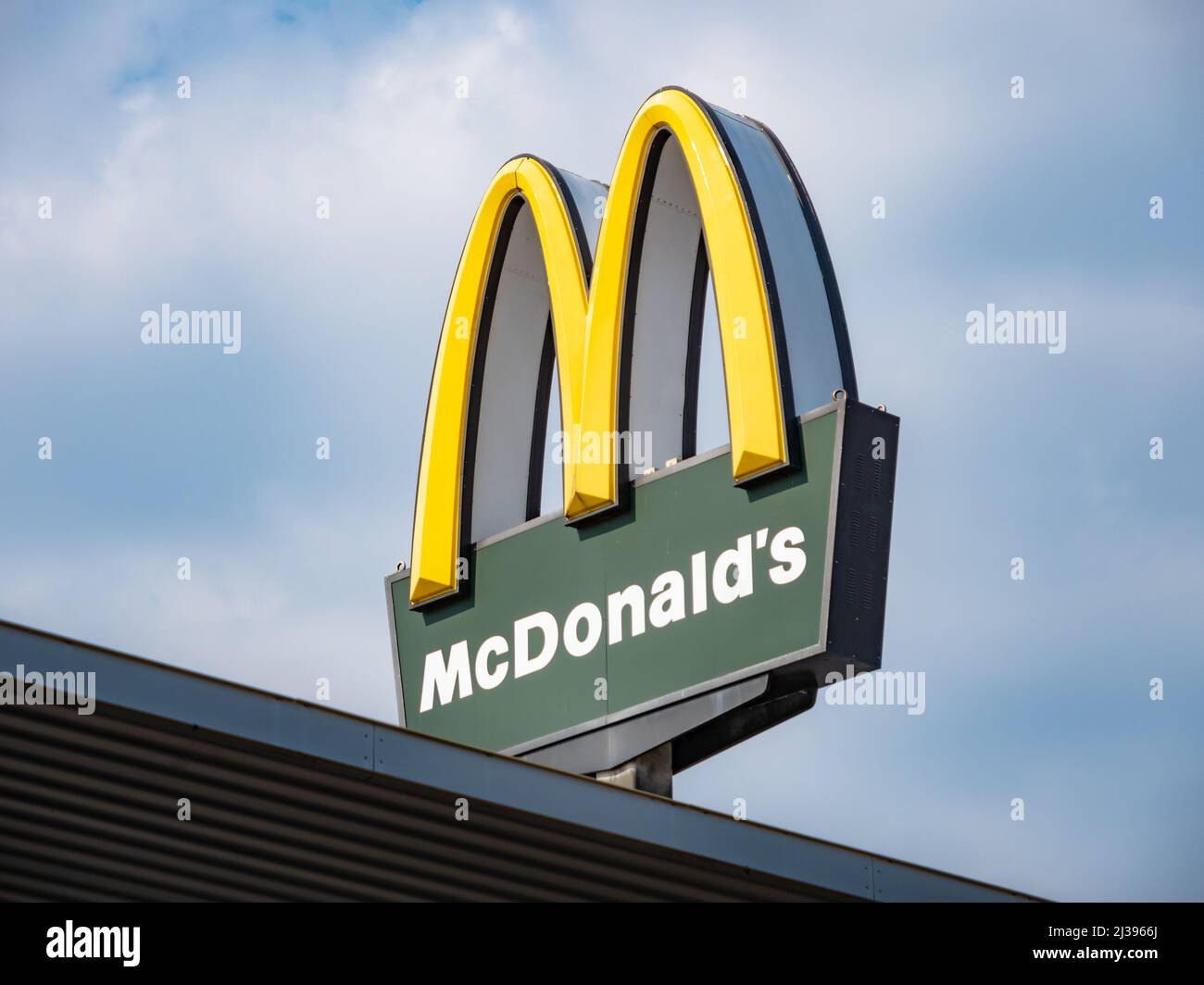 McDonald's logo on top of a restaurant. Sign on a signpost to advertise for the fast food company. American franchise business in a German city. Stock Photo