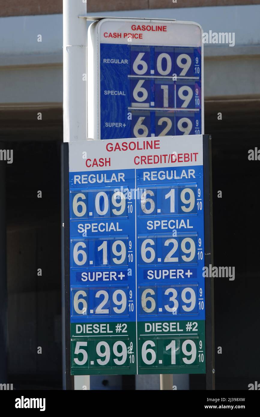 A gas station sign displays current fuel prices at over $6 USD per gallon, located next to a road in the United States during the day. Stock Photo