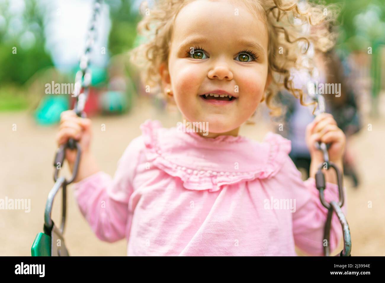 Happy little girl is playground having fun on swing Stock Photo