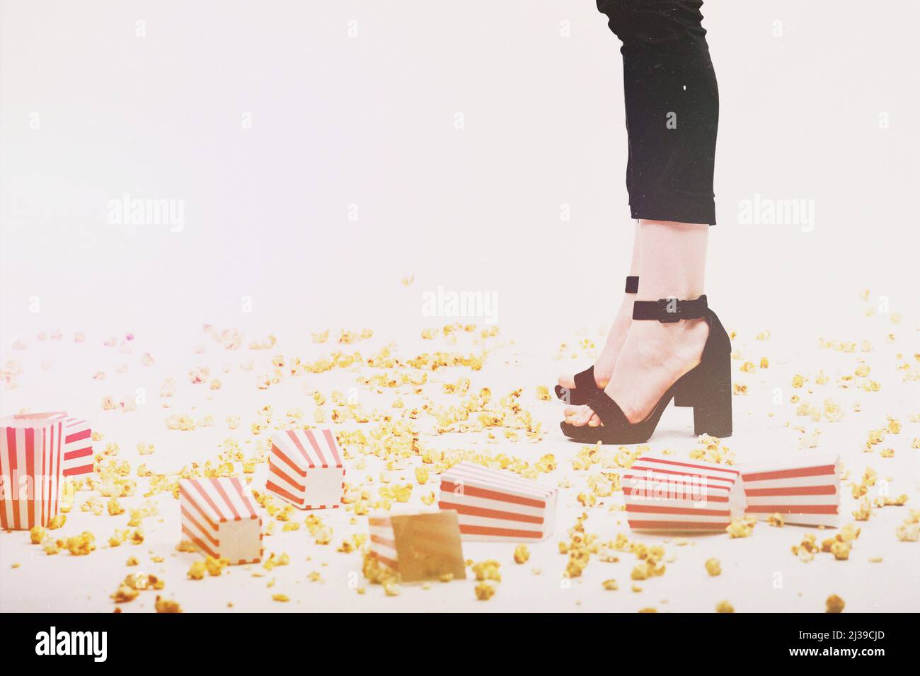 Leisure and lifestyle concept. Many popcorn and boxes tossed on floor and woman legs with black trousers and high heel shoes in white background. Vint Stock Photo