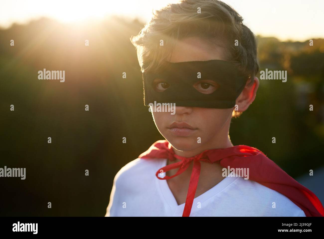 Bad guys beware. Portrait of a young boy in a cape and mask playing superhero outside. Stock Photo