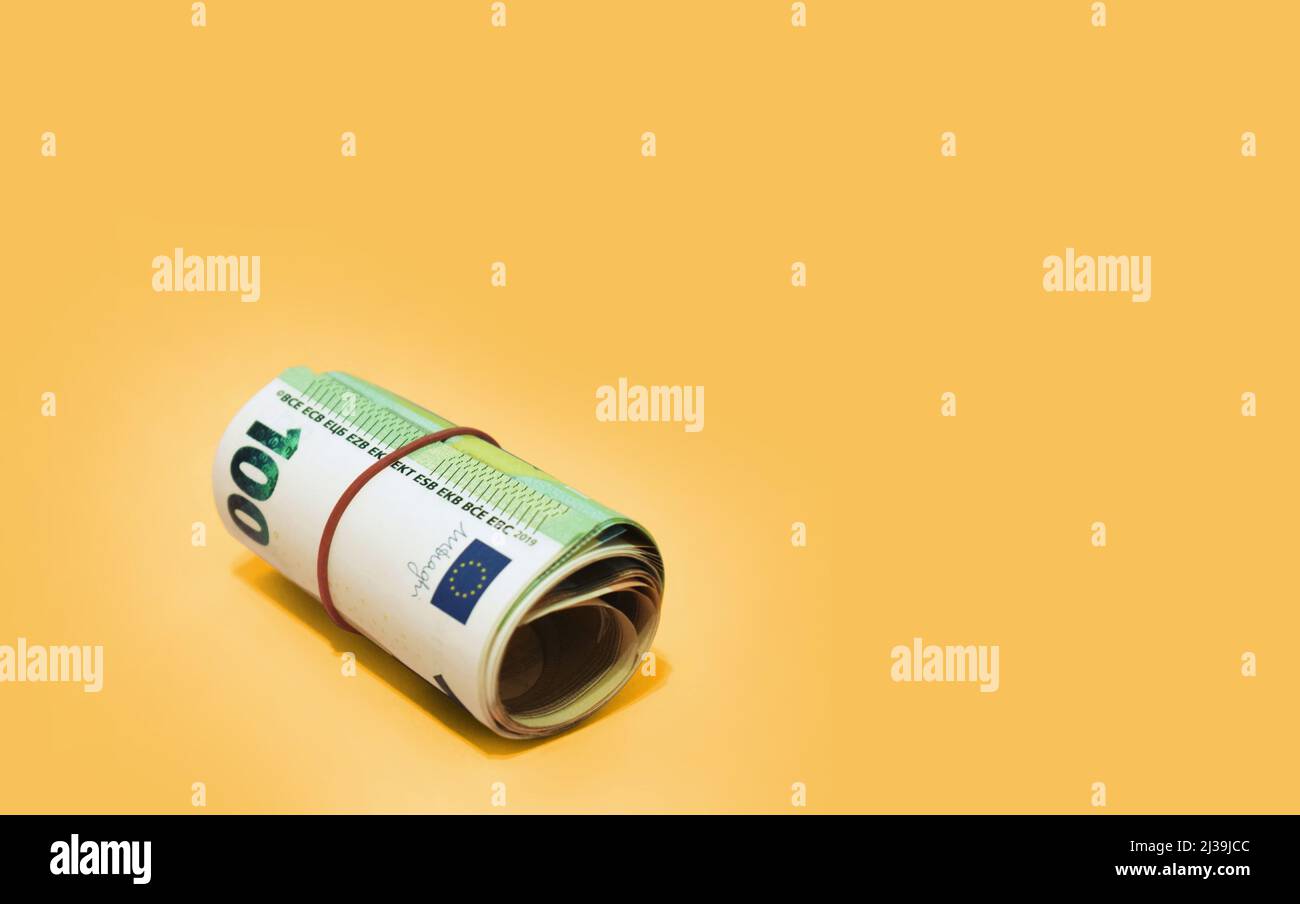 Money roll of euro banknotes with red rubber band on yellow background Stock Photo