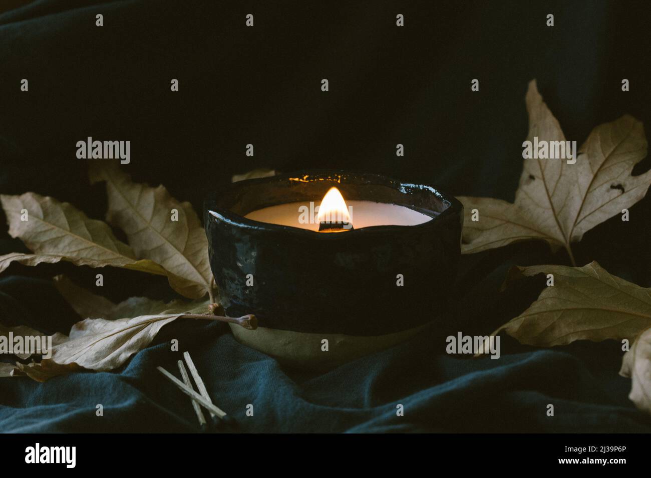 Lit wooden wick candle with fall leaves and dark background Stock Photo