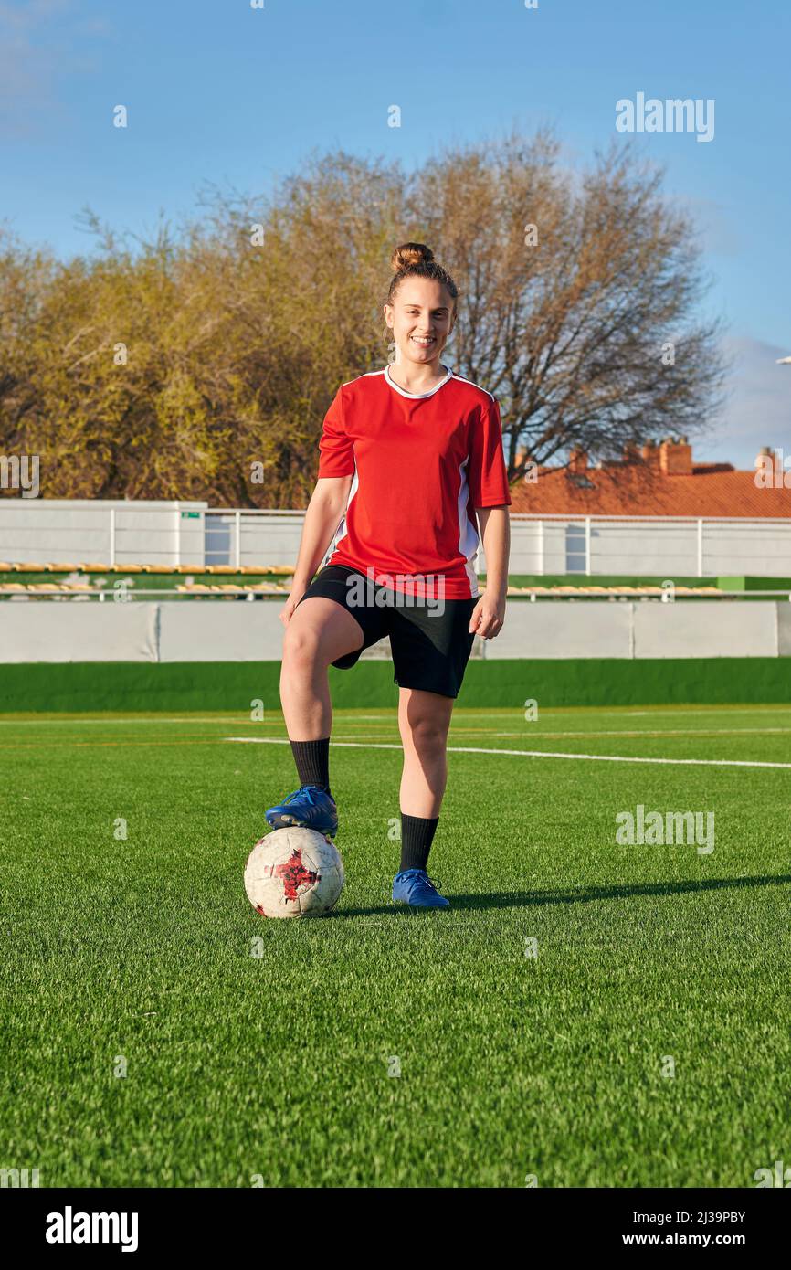 A female soccer player poses with a soccer ball looking at the camera