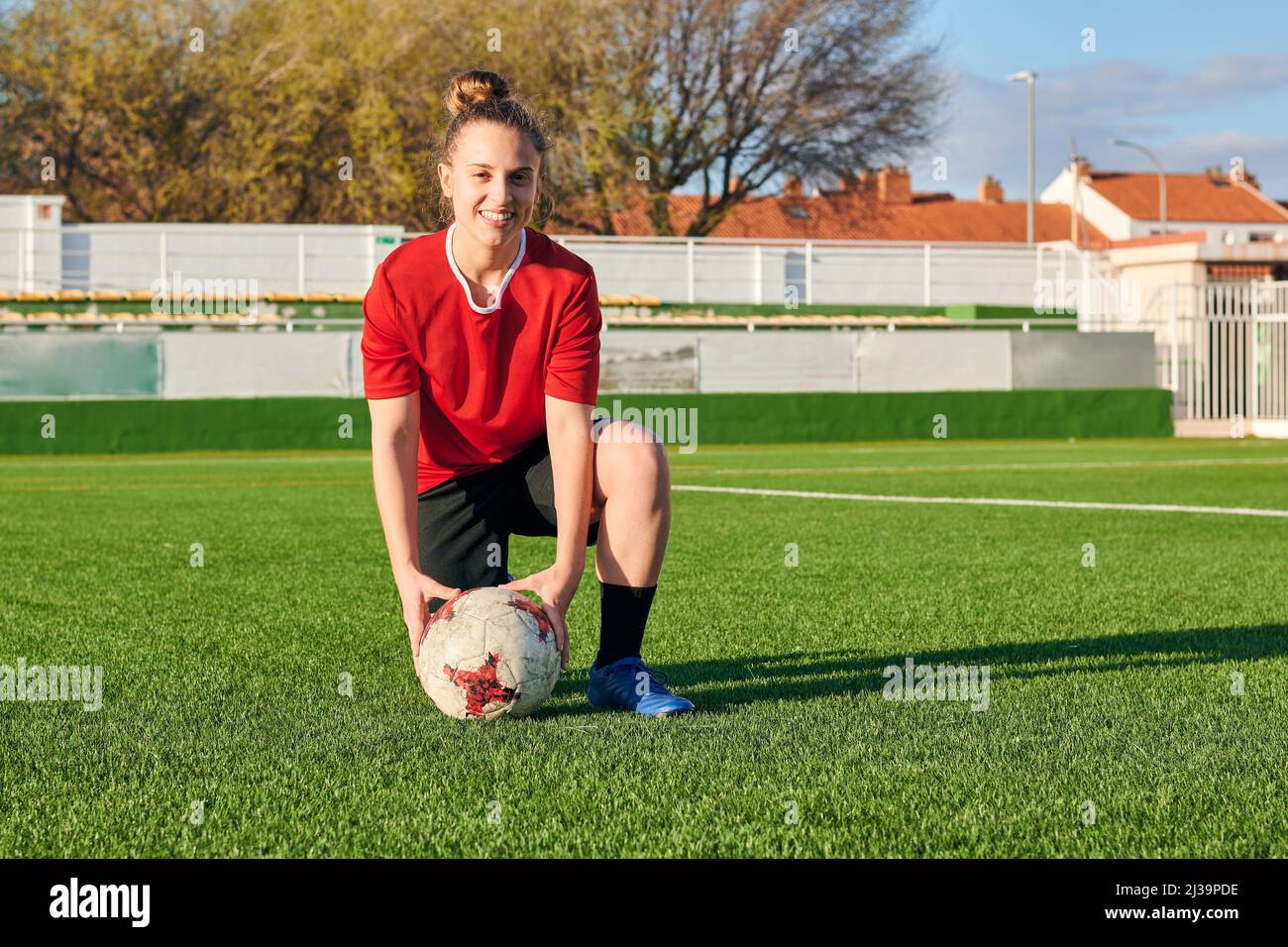 A female soccer player poses with a soccer ball looking at the camera
