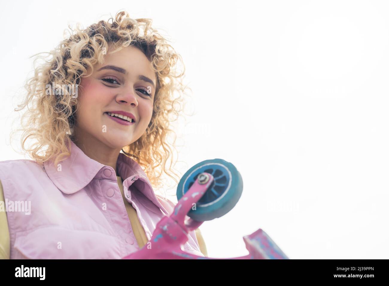 Charming young blond European woman smiling to the camera and holding a scooter, medium closeup copy space white background . High quality photo Stock Photo