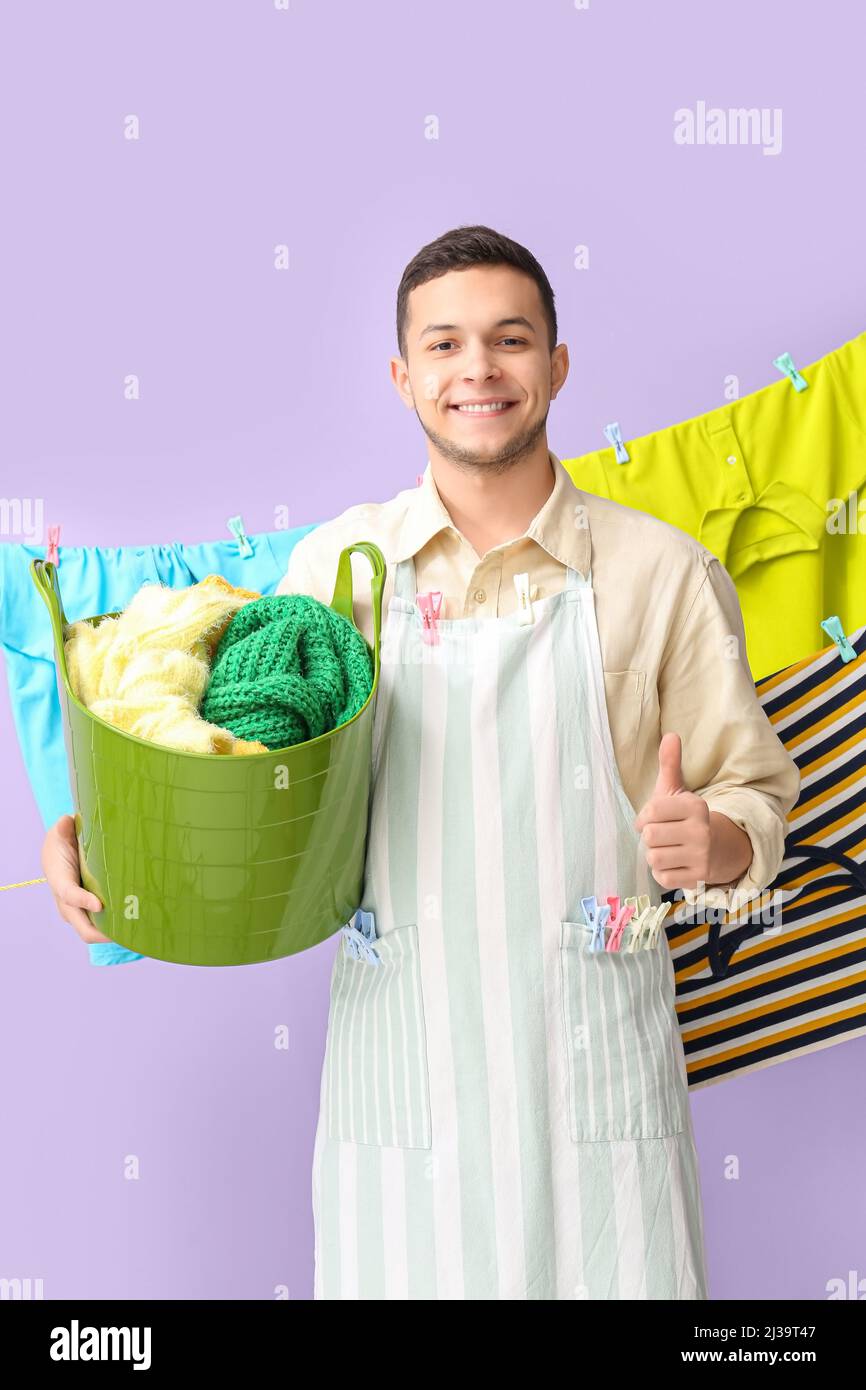 Young man with clothespins and clean laundry showing thumbup on lilac