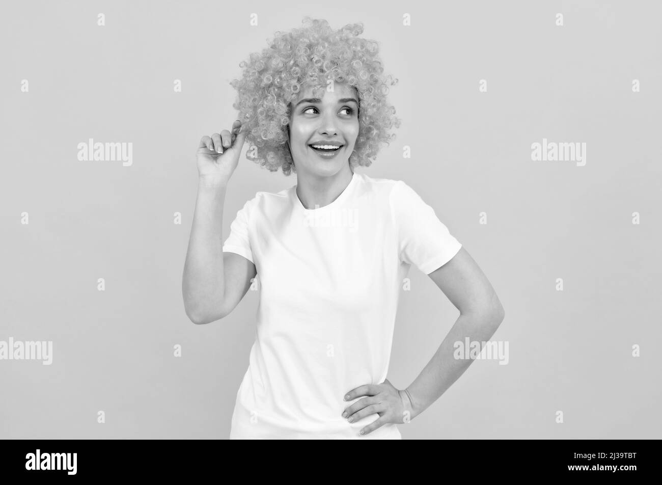 cheerful funny girl with fancy look wearing orange hair wig on yellow background, cool Stock Photo