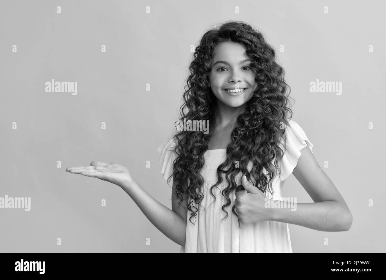happy kid with long curly hair and skin presenting product show thumb up, copy space, advertisement. Stock Photo