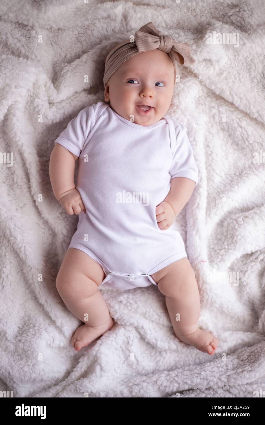 baby girl lying on a white blanket in white clothes on her stomach and