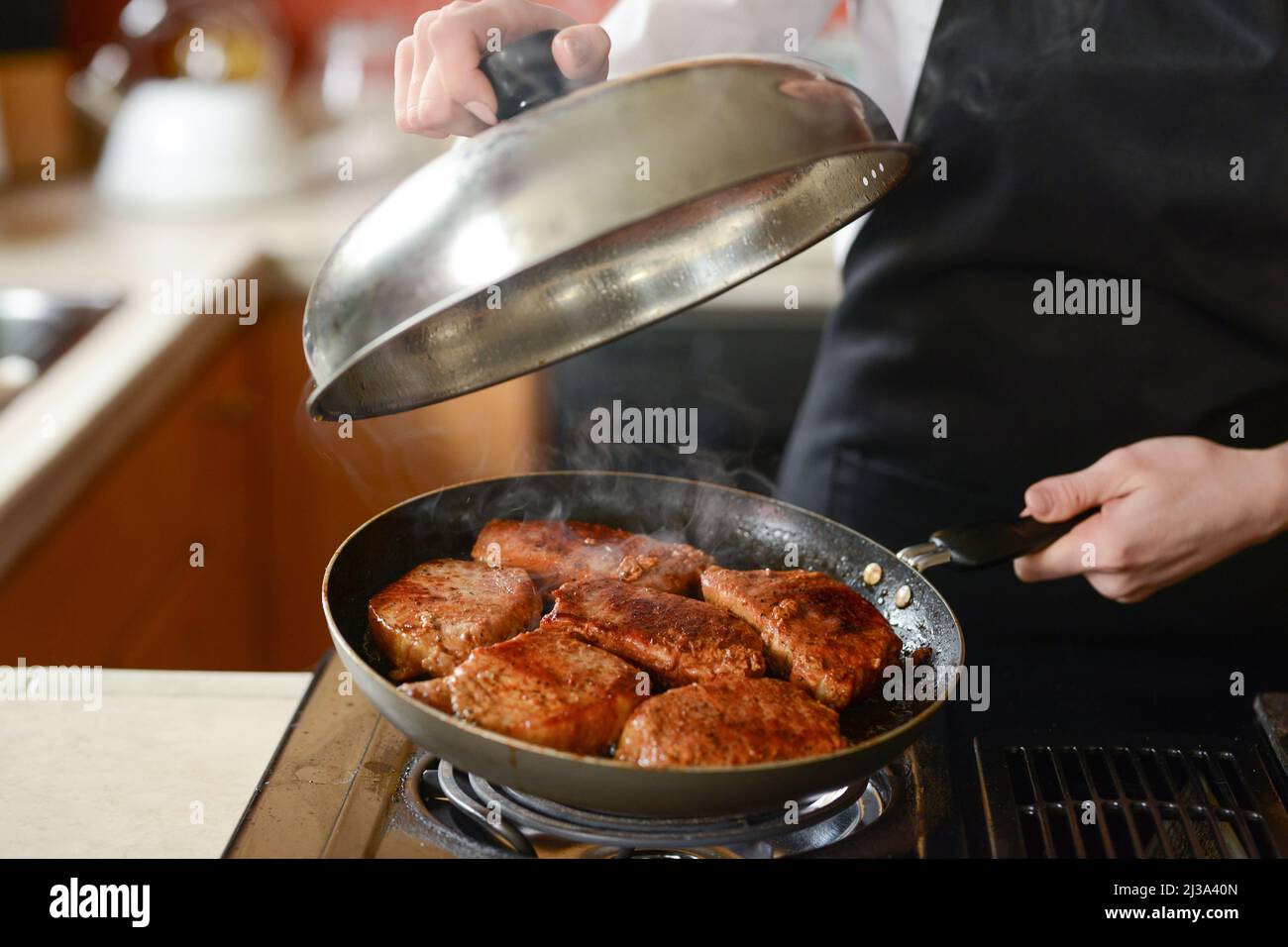 The chef in the kitchen prepares fresh pork steaks on a griddle with