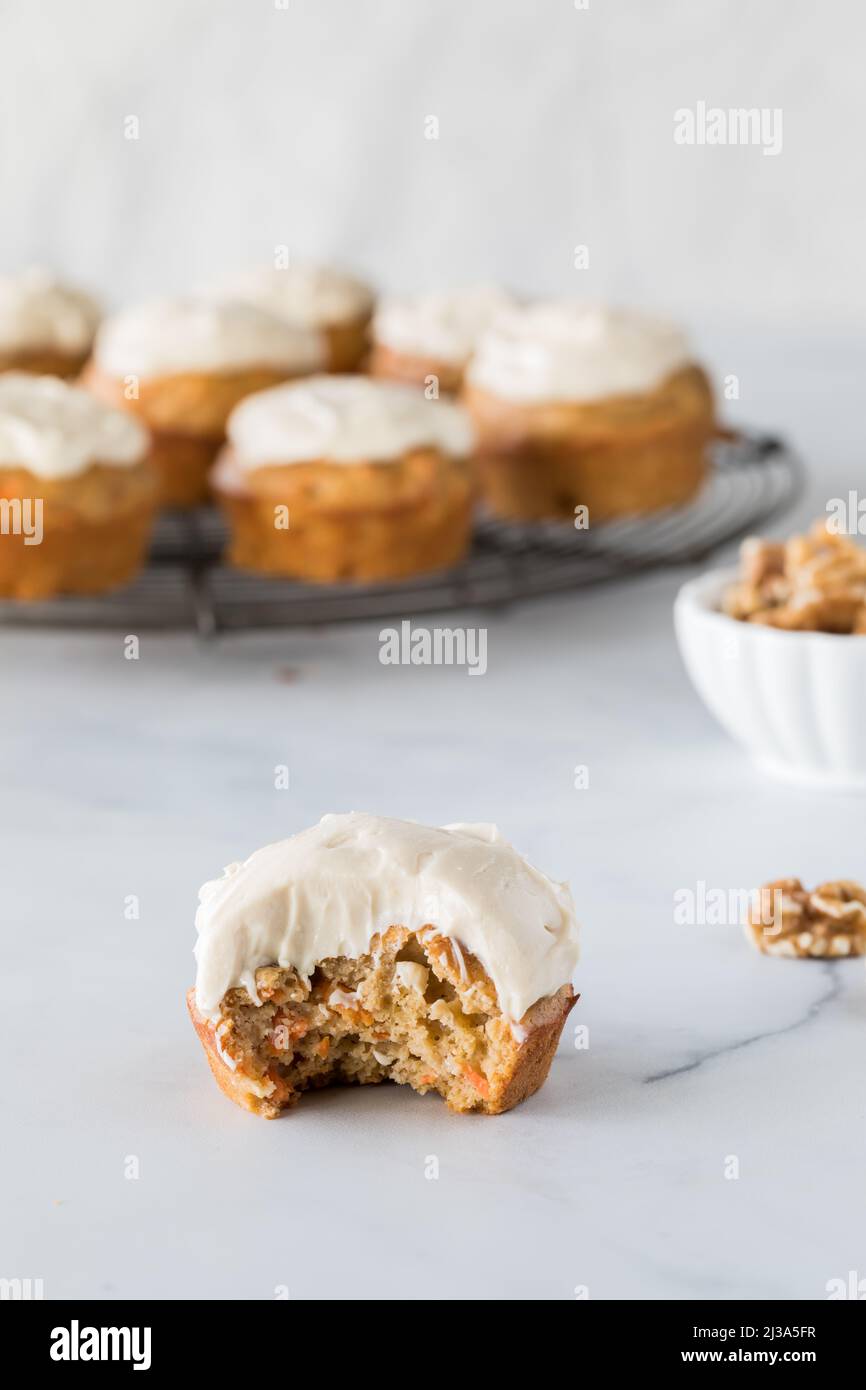 A carrot cake muffin topped with cream cheese frosting with a bite out. Stock Photo