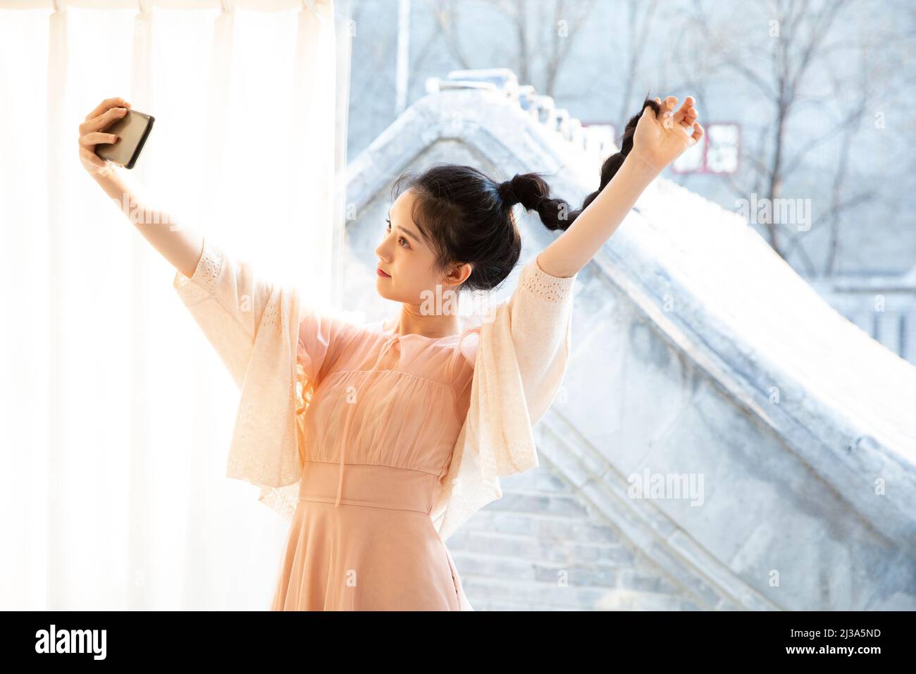 A young fashionable woman spends her leisure time looking at herself in the mirror using her mobile phone selfie function - stock photo Stock Photo