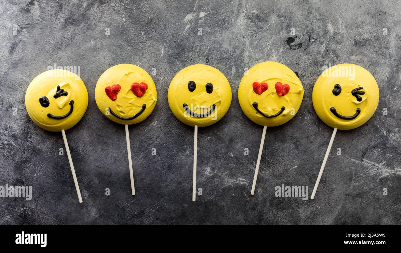 A row of smiley face emoji merengues on lollipop sticks. Stock Photo