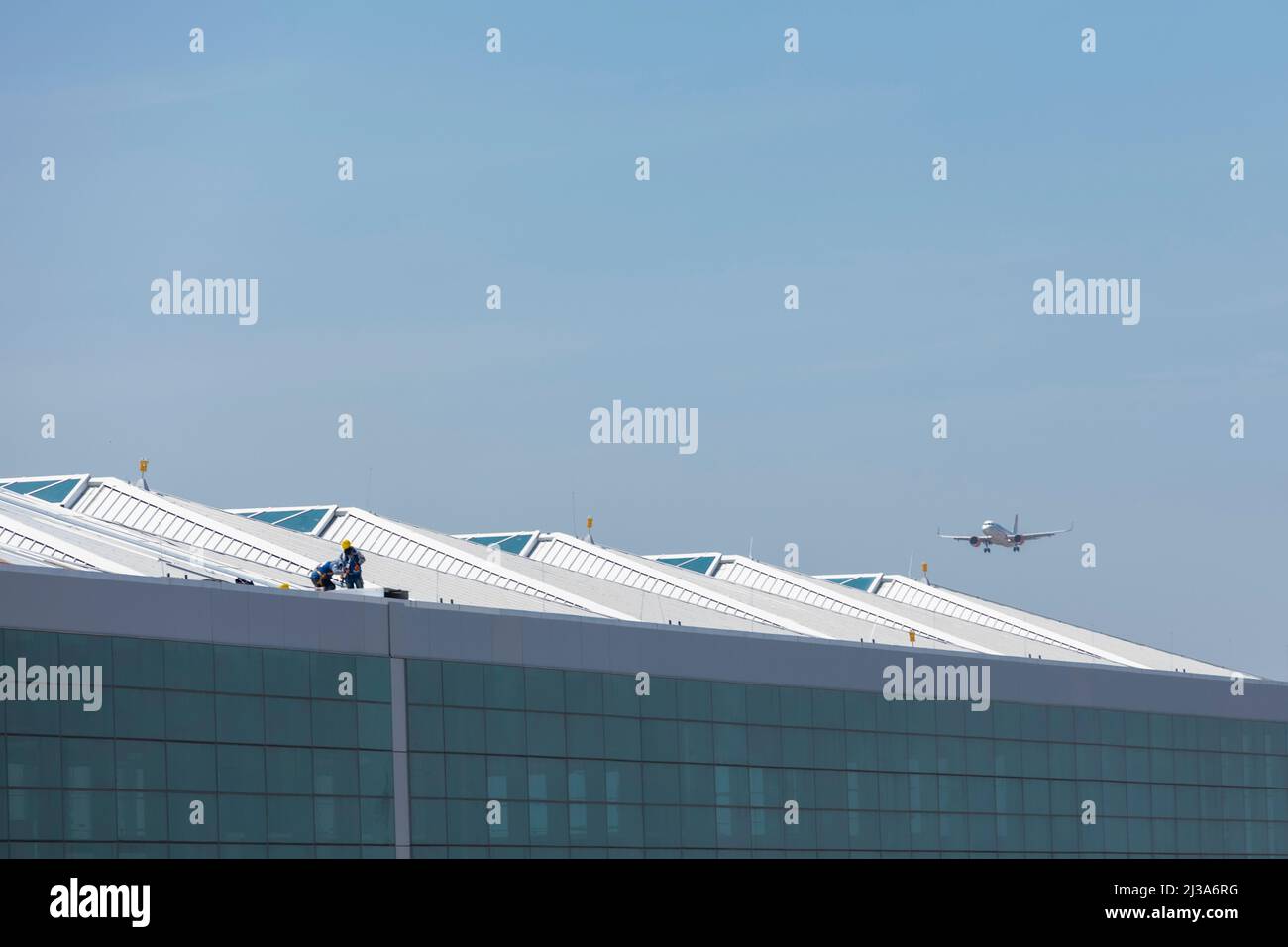 Aspect of the Felipe Angeles International Airport. Workers on the roof while a plane lands in. Stock Photo