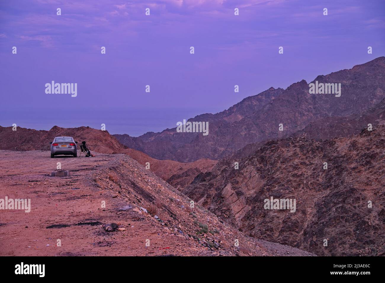 Woman sitting by car at the edge of canyon Stock Photo