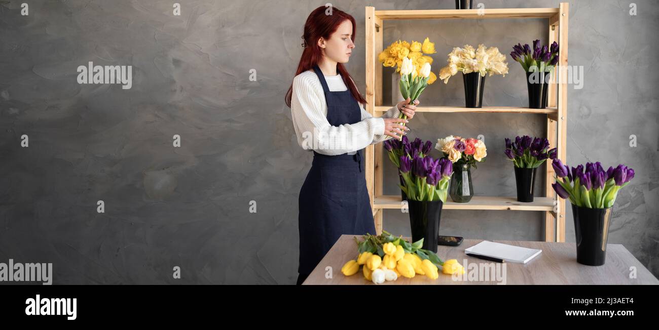 Florist at work a pretty young woman in an apron makes a trendy modern bouquet of tulip flowers.Baner. Stock Photo