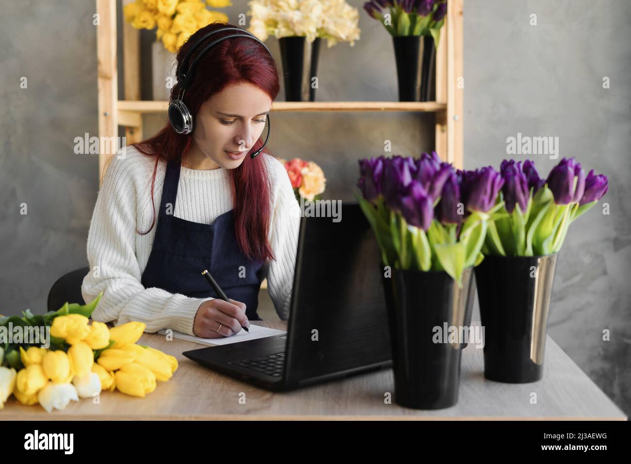 Young woman florist in blue apron business owner using headset and