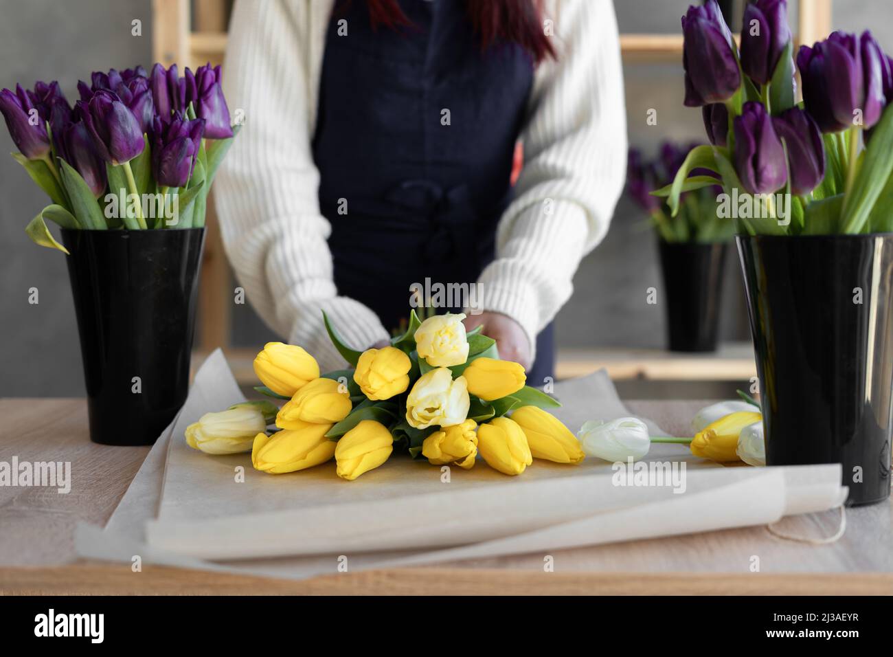 Close-up of female hands make a bouquet of tulips. Florist workplace. Preparing a gift for a loved one. Stock Photo
