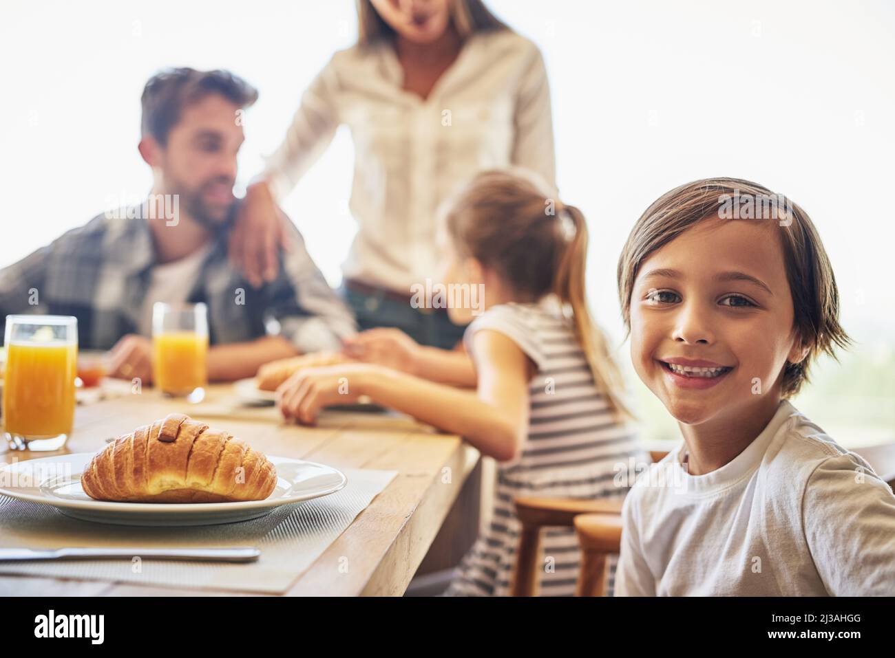 Were filling our tummies for the day ahead. Portrait of a little boy having breakfast with his family in the background. Stock Photo