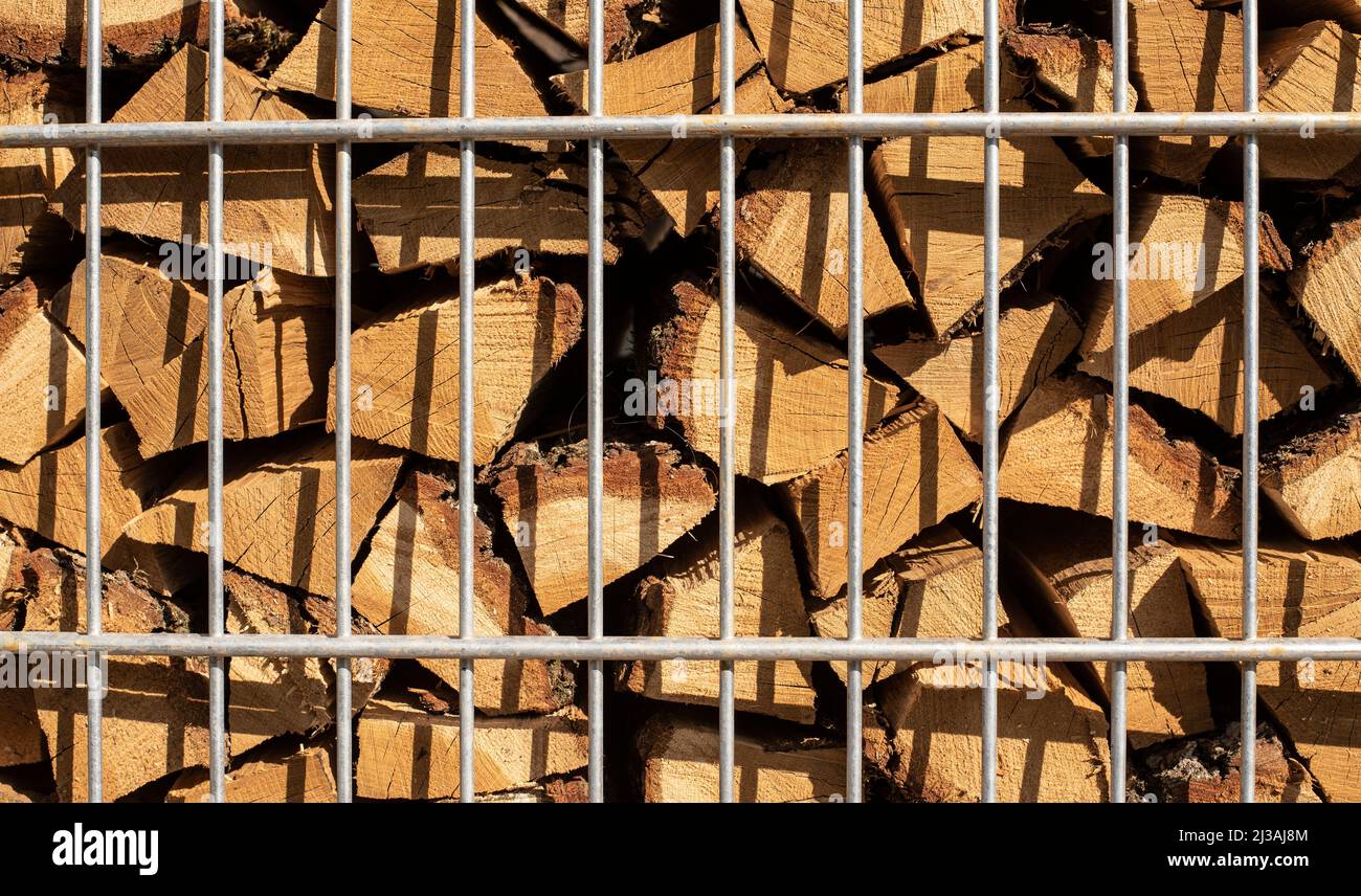 a stack of cut fuel wood behind a metal fence in sunlight Stock Photo ...