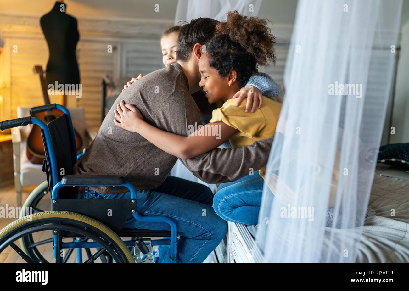 Happy family. Smiling father with disability in wheelchair hugging with children at home Stock Photo