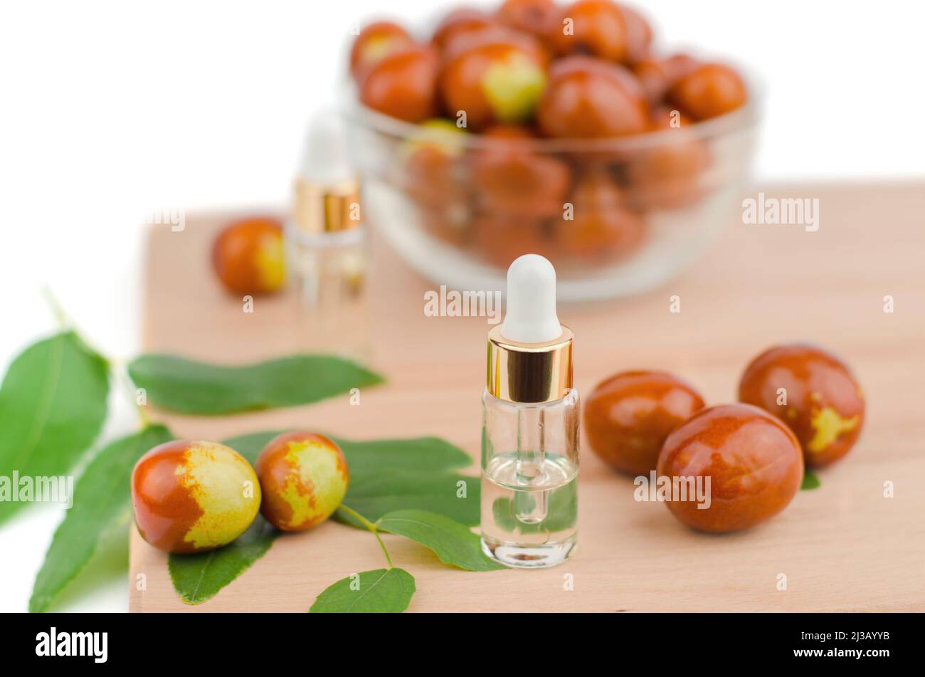 Jojoba oil in a transparent bottle with a dropper and fresh jojoba fruit on a wooden table. Chinese date fruit and oil Stock Photo