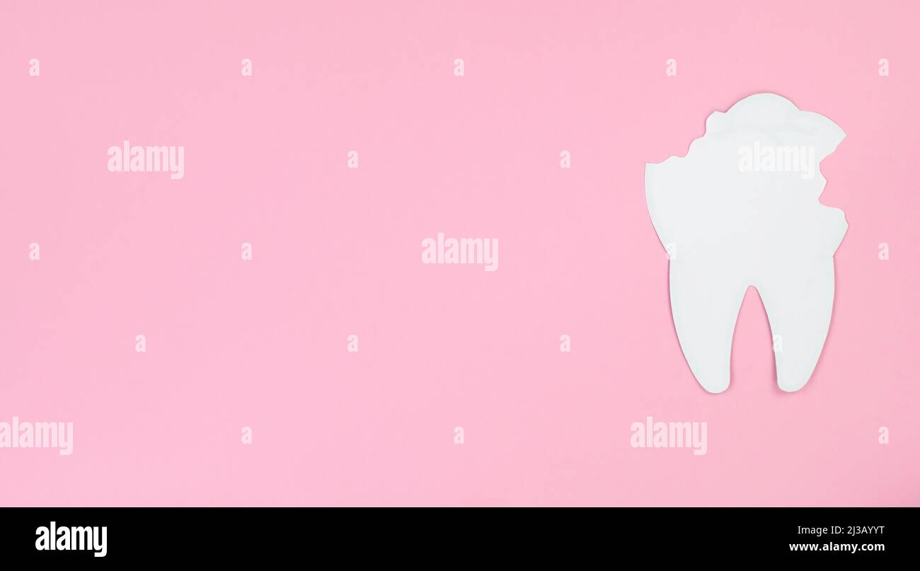 White paper tooth with caries on a pink background, space for text