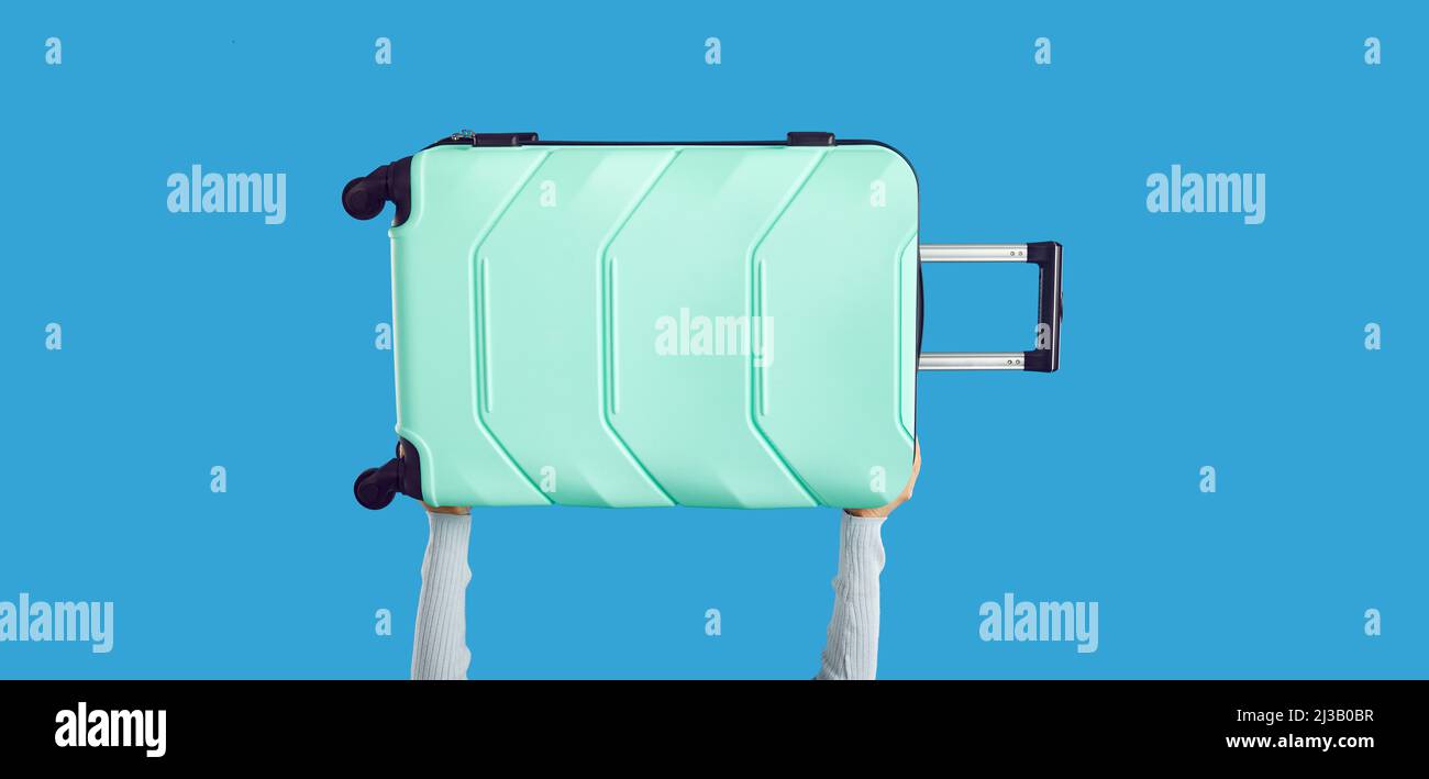 Anonymous person holding up carry-on holiday luggage isolated on blue background Stock Photo