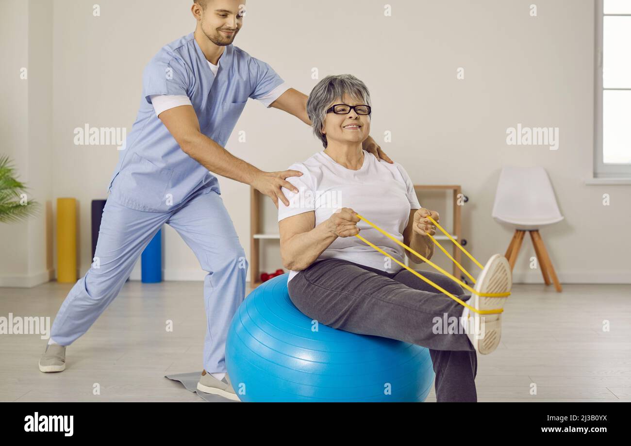 Doctor helping senior woman with osteoporosis do exercises with rubber band and fitball Stock Photo